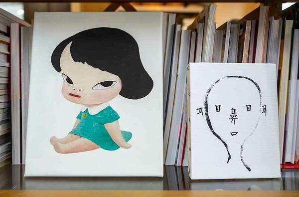 Artwork of a doll like child and an outline of a face lean up against shelf of books.