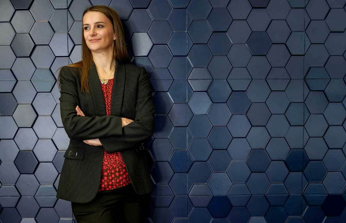 A woman poses against a blue hexagon-pattern wall.
