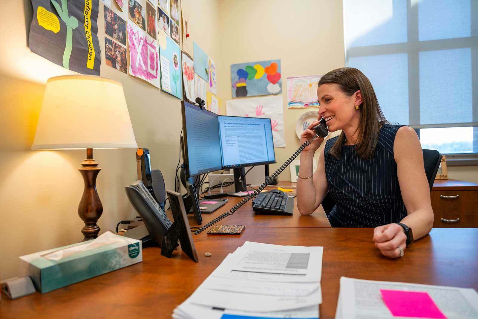 A woman talks on a phone at an office desk.